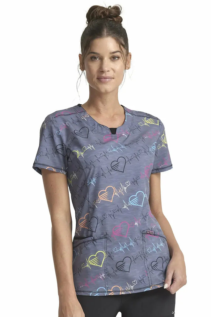 A young female Pediatric Nurse wearing a Cherokee Infinity Woman's Round Neck Printed Scrub Top in "Pop Beats" size XS featuring a contemporary fit.