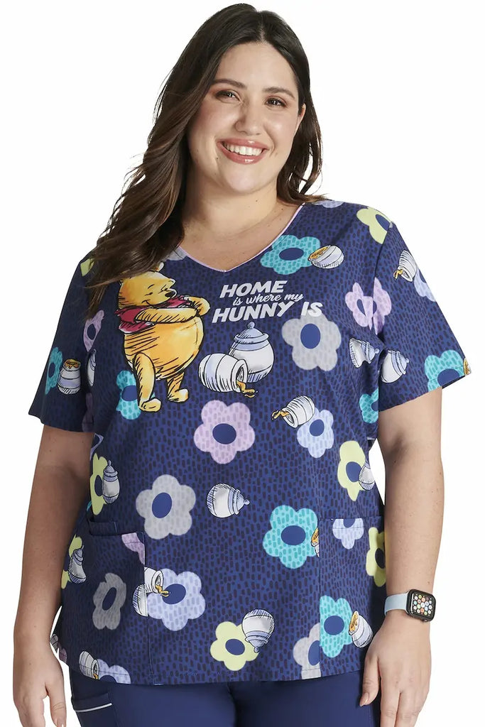 A young female Neonatal Nurse wearing a Tooniforms Women's V-neck Printed Scrub Top in "Home And Hunny" size 3XL featuring bust darts and side slits to provide a flattering and comfortable all day fit. 