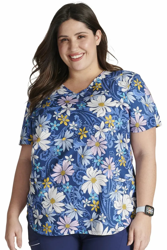 A young female Pediatric Nurse wearing a Cherokee Women's V-neck Printed Scrub Top in "Prairie Paisley" size 3XL featuring a charming print with intricate paisley patterns in a vibrant color palette, adding a touch of personality and elegance.
