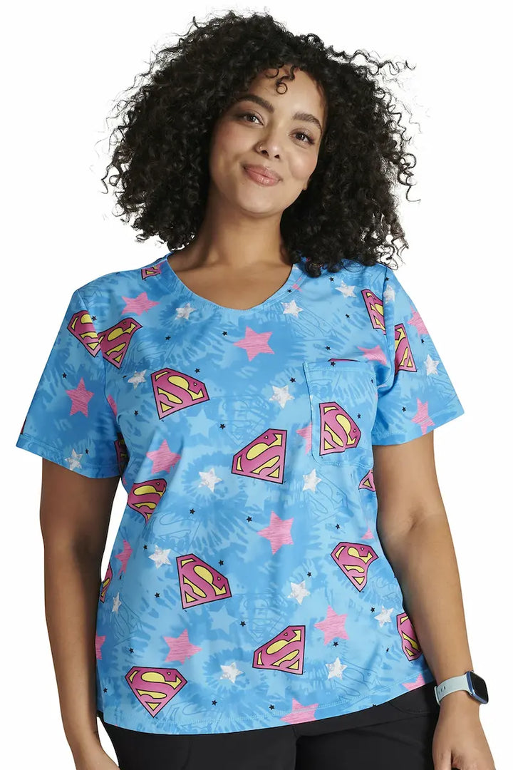 A young female Pediatric Nurse wearing a Tooniforms Women's Rounded V-neck Printed Scrub Top in "Symbol of Hope" size 2XL featuring a contemporary fit.