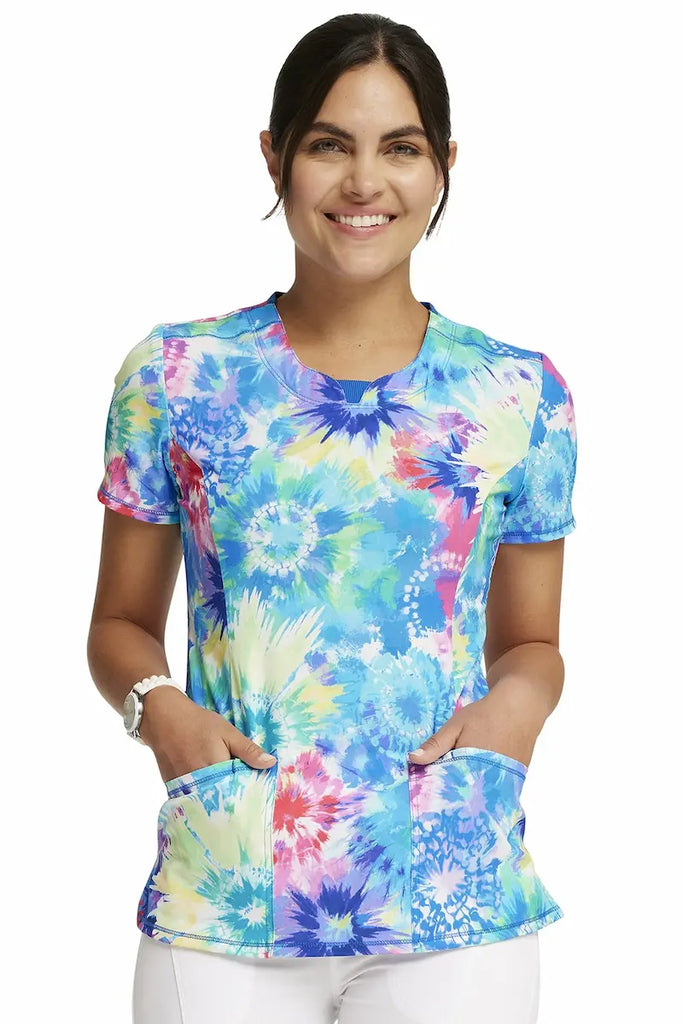 A young female Oncology Nurse wearing a Cherokee Infinity Women's Round Neck Printed Scrub Top in "Tie Dye Burst" size XL featuring two front patch pockets for ample storage space.