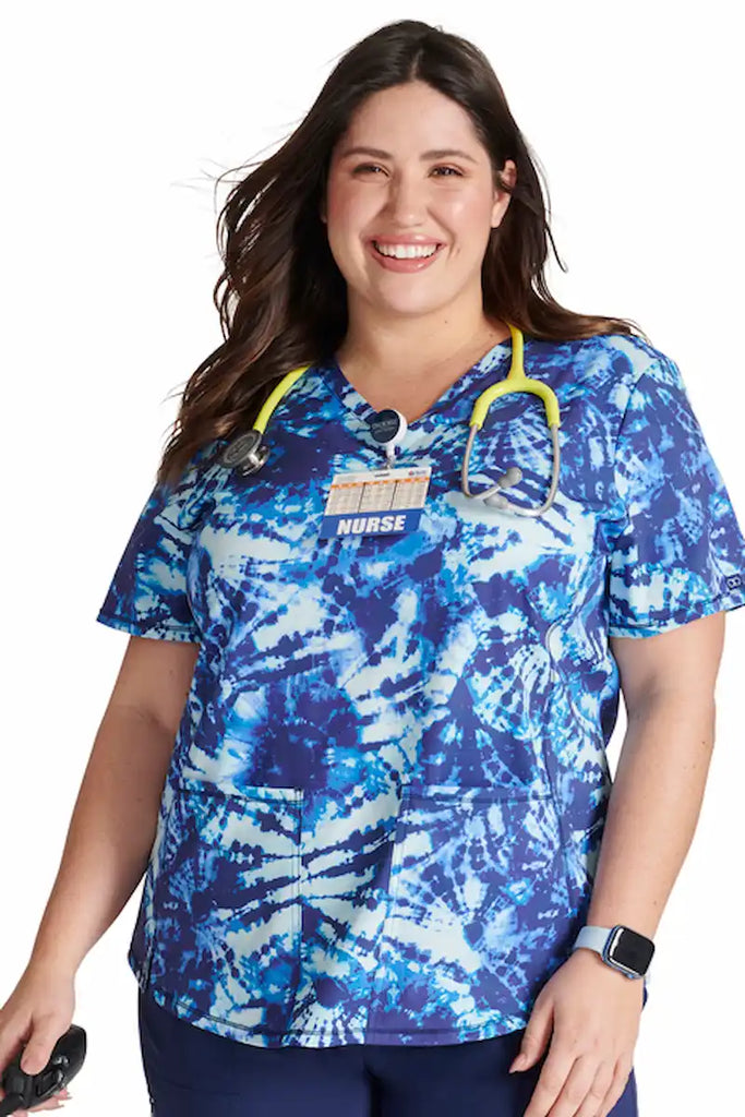 A young female Neonatal Nurse wearing a Cherokee Women's V-neck Printed Scrub Top in "Tie Dye Tranquility" size 2XL featuring a contemporary fit.