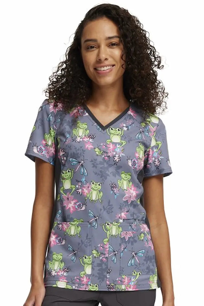 A young female Pediatric Nurse wearing a Cherokee iFlex Women's V-neck Knit Panel Printed Scrub Top in "Toad-ally Floral Friends" size Small featuring a modern classic fit.