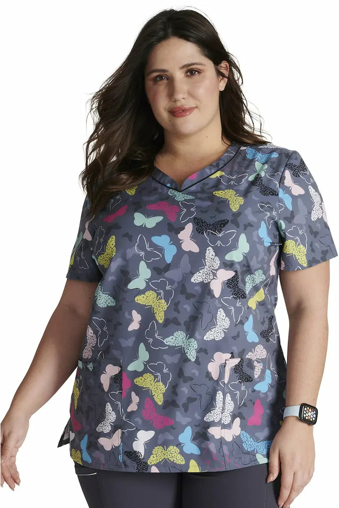 A young female Pediatric Nurse wearing a Cherokee V-neck Printed Scrub Top in "Wing It Up" size 3XL featuring a modern classic fit.