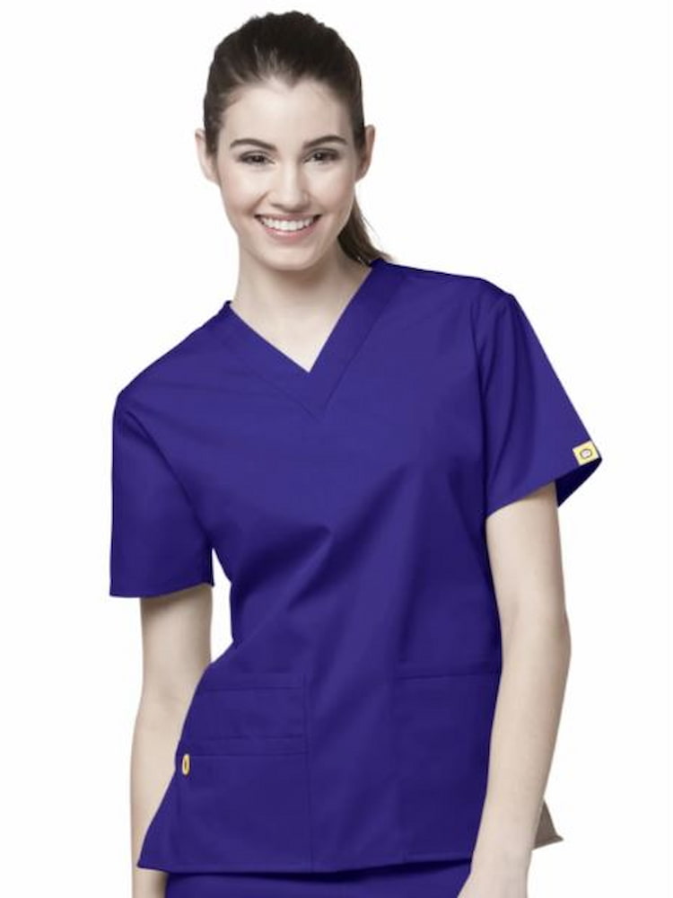 A young female Physical Therapist's Assistant wearing a WonderWink Women's Bravo V-neck Scrub Top in Grape size 3XL featuring a modern fit, vented sides and a total of 5 pockets.
