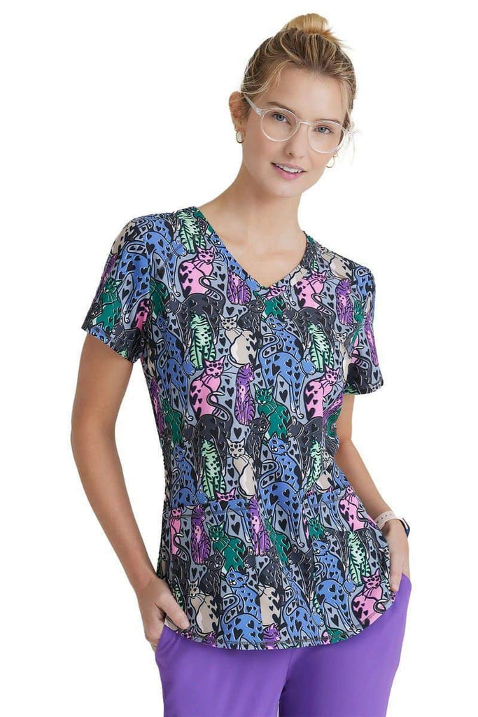 A young female Veterinarian wearing a Skechers BOBS Women's Printed Scrub Top in "Hearts on Hearts" featuring two front patch pockets.