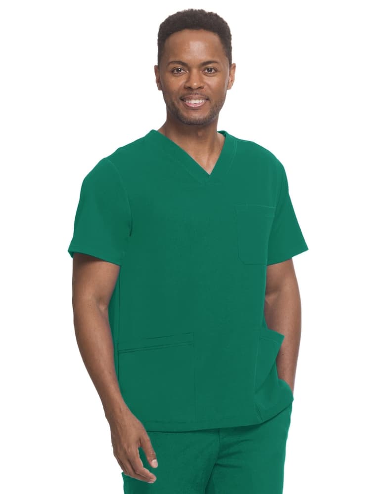 A young male Surgical Technician wearing an HH-Works Men's Matthew V-neck Scrub Top in Hunter Green featuring 2 large patch pockets & 1 chest pocket for your necessities.