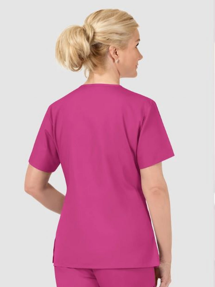 A middle aged female Nursing Assistant wearing a WonderWink Women's Bravo Scrub Top in Hot pink size Medium featuring a soft poly cotton blend.