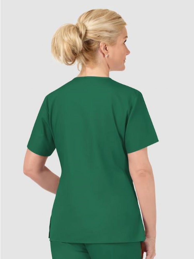 A middle aged female surgeon wearing a WonderWink Origins Women's Bravo V-neck Scrub Top in Hunter Green sized Large featuring vents  at the side.