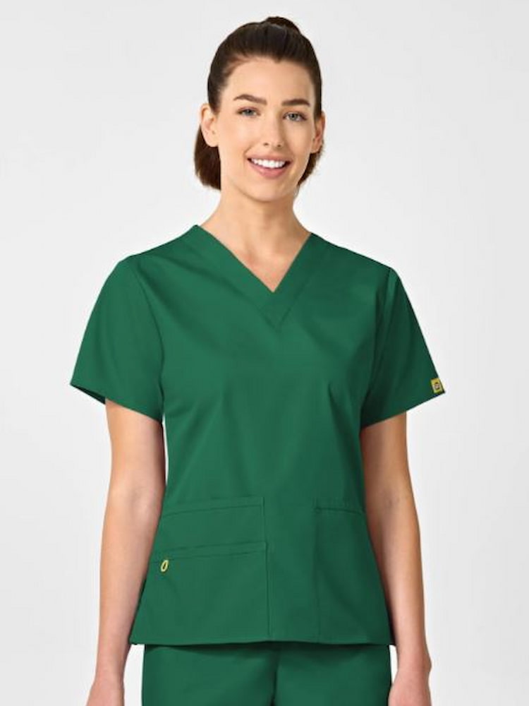 A young female Surgical Assistant wearing a WonderWink Origins Women's Bravo Scrub Top in Hunter Green size XS featuring a modern fit.