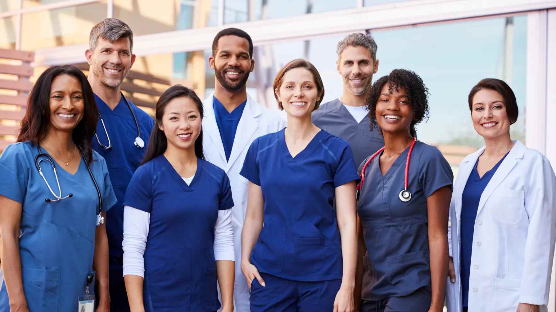 A group of Nurses, Physicians, and Medical Technologists wearing Navy Blue scrub Uniforms outside of a hospital.