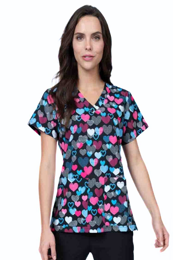 A young female Nurse Practitioner wearing a Meraki Sport Women's Print Scrub Top in "Follow Your Heart" featuring a v-neckline & short sleeves.