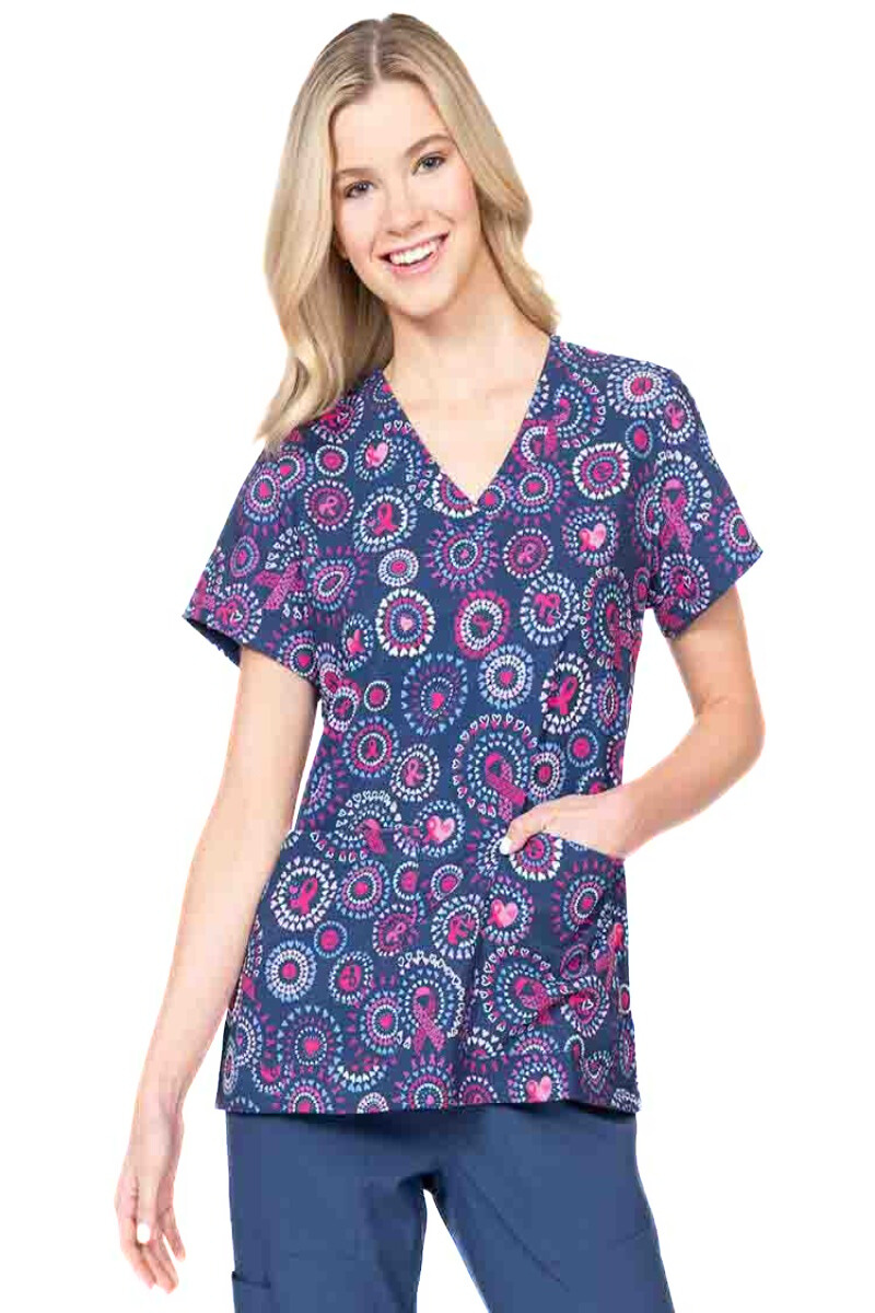 A young female Nurse Practitioner wearing a Meraki Sport Women's Print Scrub Top in "Girl Power" featuring a v-neckline & short sleeves.