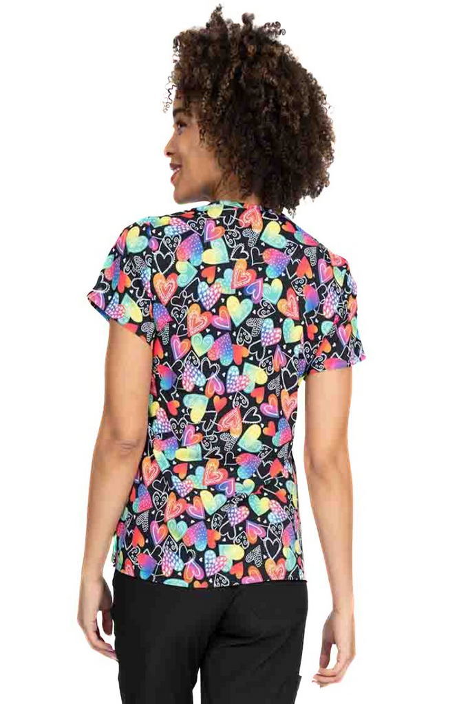 A young lady nurse wearing a Meraki Sport Women's Print Scrub Top in "Wild at Heart" featuring shoulder yokes & side slits for additional range of motion.