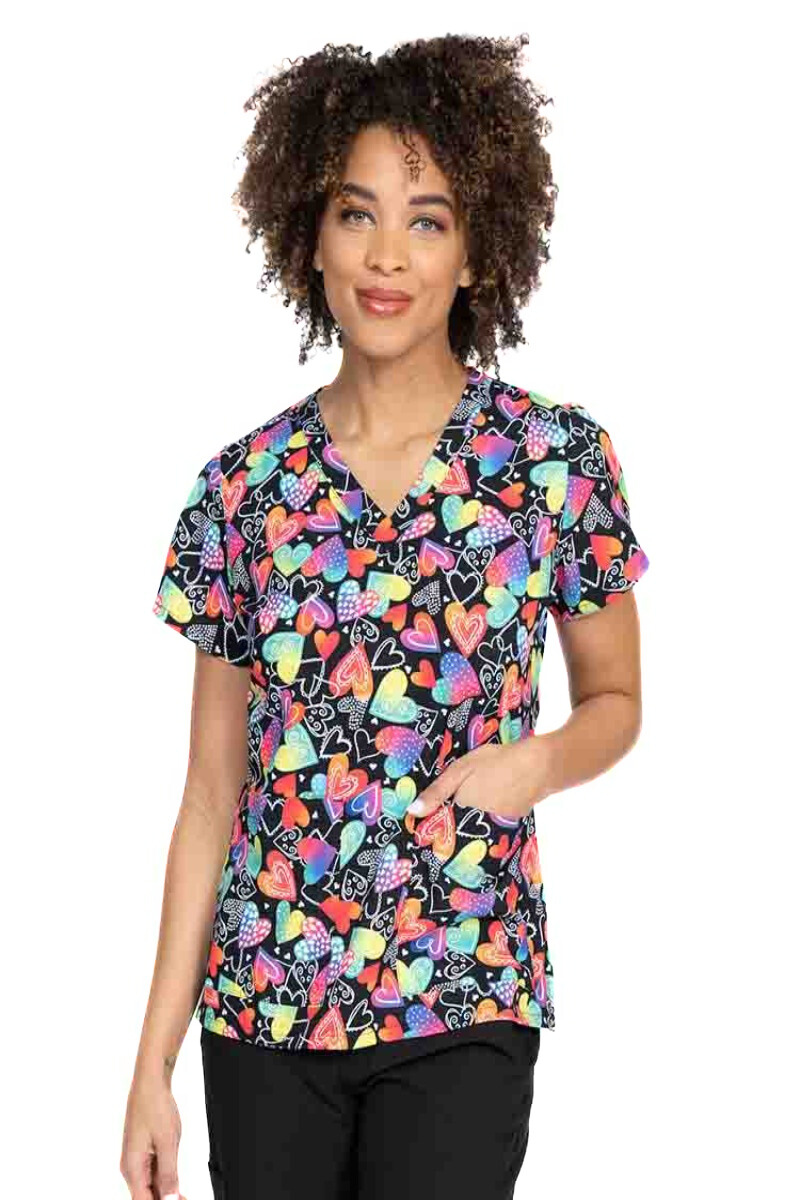 A young female Nurse Practitioner wearing a Meraki Sport Women's Print Scrub Top in "Wild at Heart" featuring a v-neckline & short sleeves.