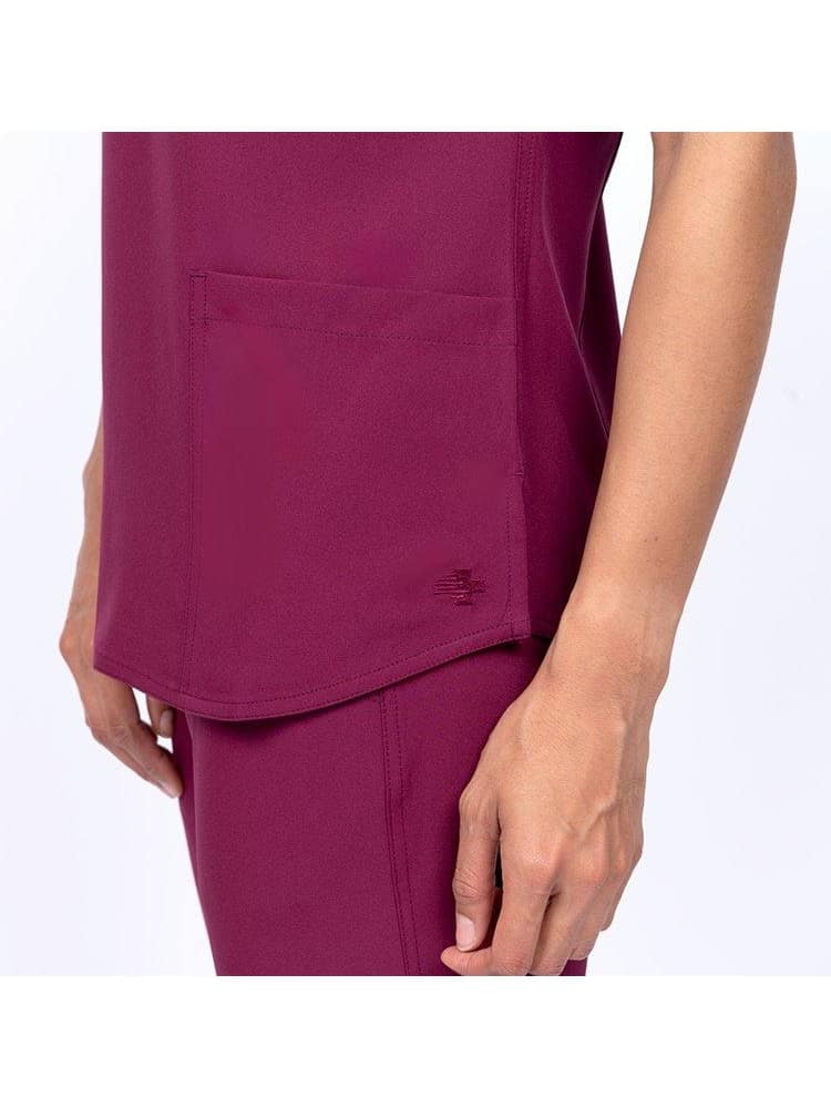 A young female Physician's assistant wearing a Meraki Sport Women's V-neck Scrub Top in Wine size Medium featuring side slits for additional range of motion.