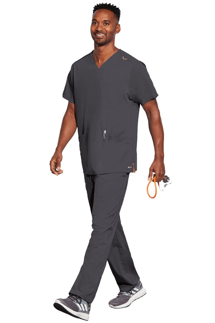 A young male CNA wearing a Barco Motion Unisex V-Neck Scrub Top in Pewter size Medium featuring 2 front patch pockets for all your on the job storage needs.