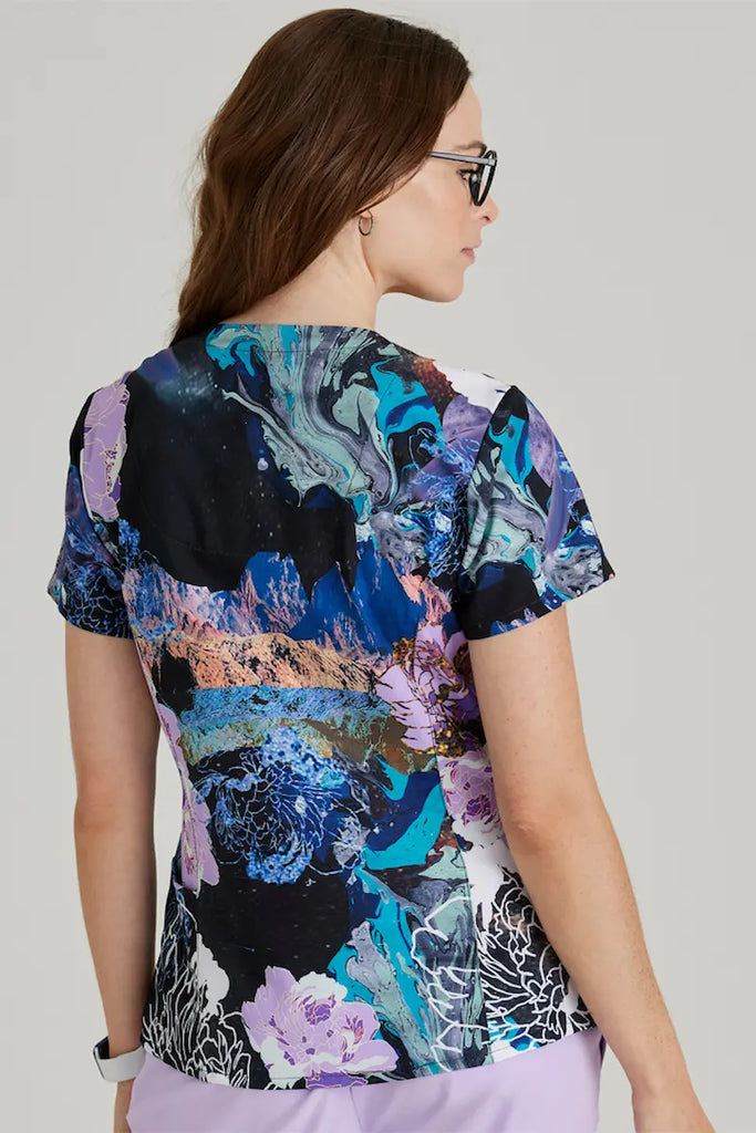 A female psychiatric nurse showcasing the back of the Barco One Women's Print Scrub Top in Mystic Flower featuring a center back length of 27.75".