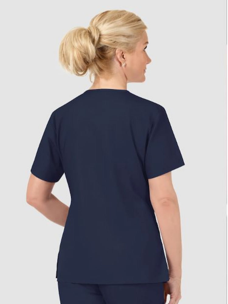 A middle aged female Registered Nurse wearing a WonderWink Origins Women's Bravo Scrub Top in Navy size Medium featuring side vents for additional mobility.