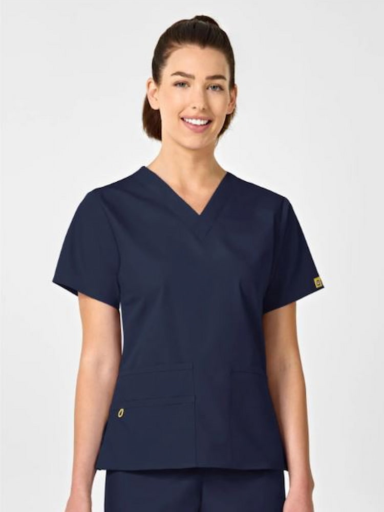 A young female Physician's Assistant wearing a WonderWink Origins Women's Bravo V-neck Scrub Top in Navy size XL featuring a soft poly cotton blend.