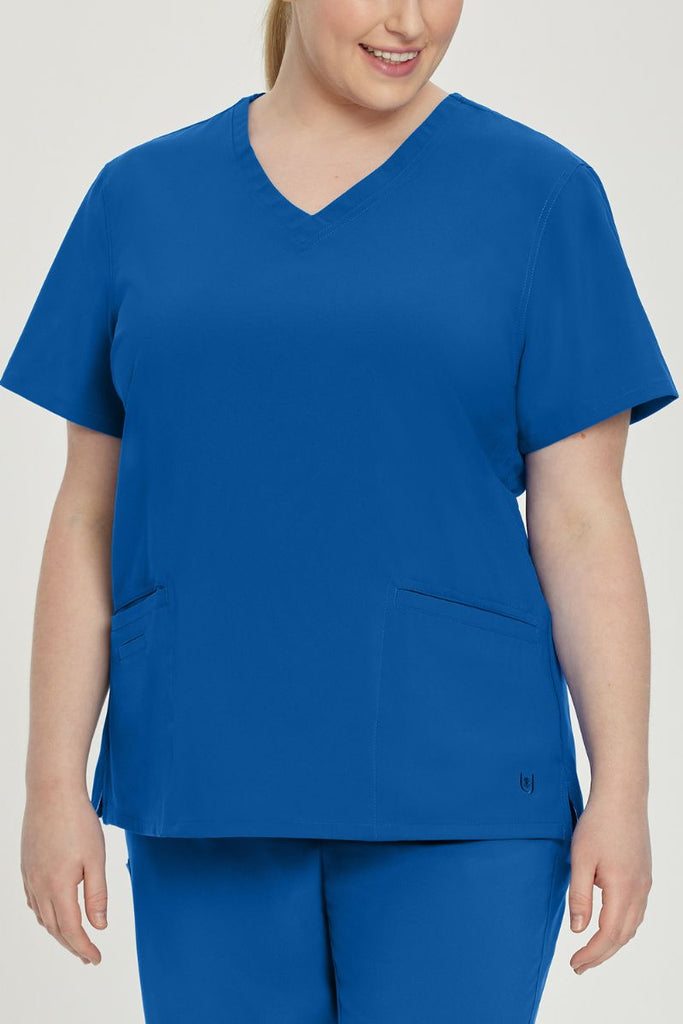 A young female Physical Therapy Aide wearing an Urbane Performance Women's Motivate V-neck Scrub Top in New Royal size 4XL featuring tonal stitching and bust darts.