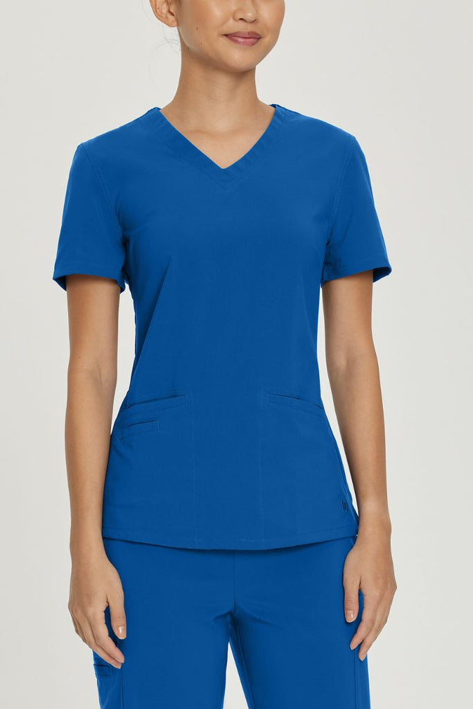 A young female LPN wearing an Urbane Performance Women's Motivate V-neck Scrub Top in New Royal size Large featuring a two front angled welt pockets.