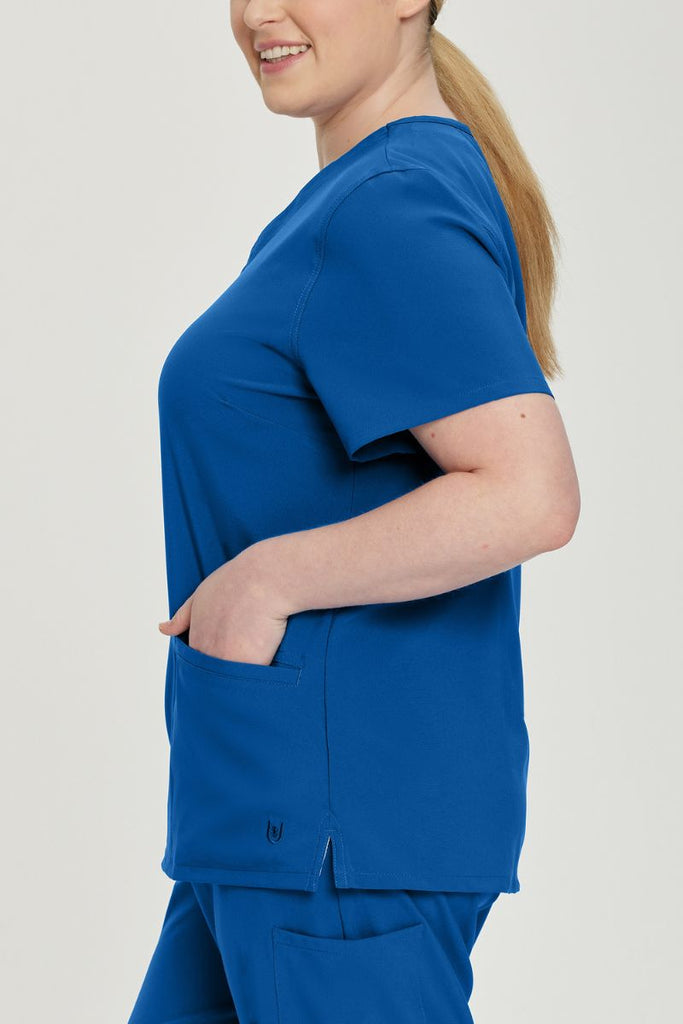 A young female Doctor wearing an Urbane Performance Women's Motivate V-neck Scrub Top in Royal Blue featuring a total of 3 pockets.