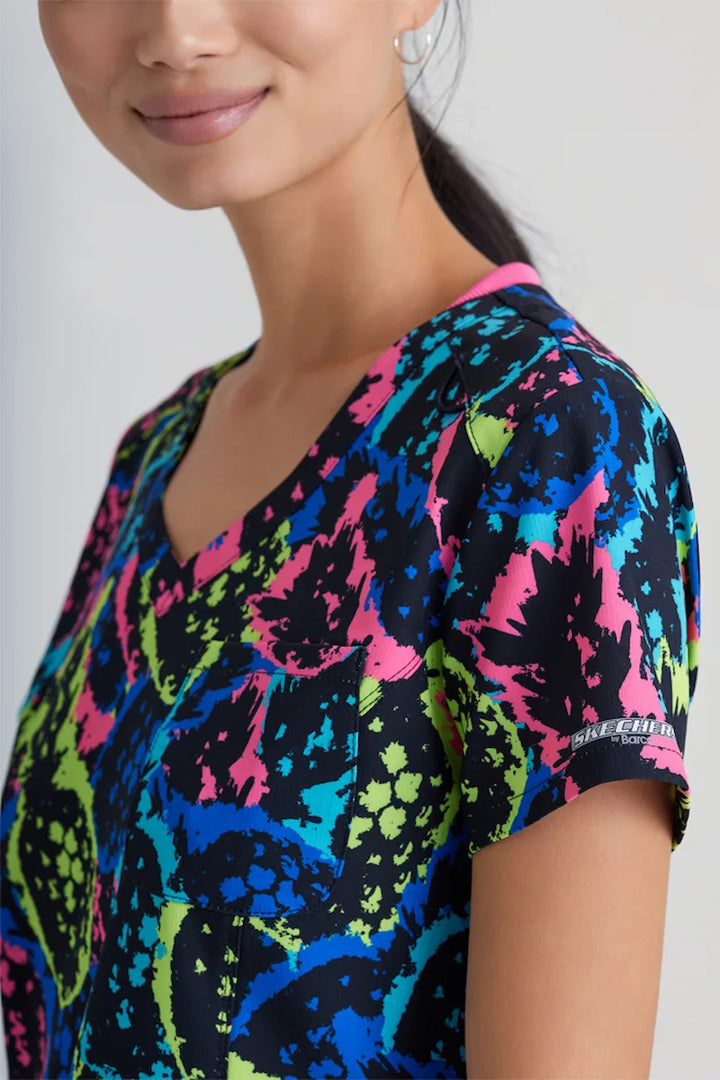 A close look at the side of the Skechers Women's Printed V-Neck Scrub Top in Pineapple Pop featuring the Skechers Logo printed on the side of the sleeves.