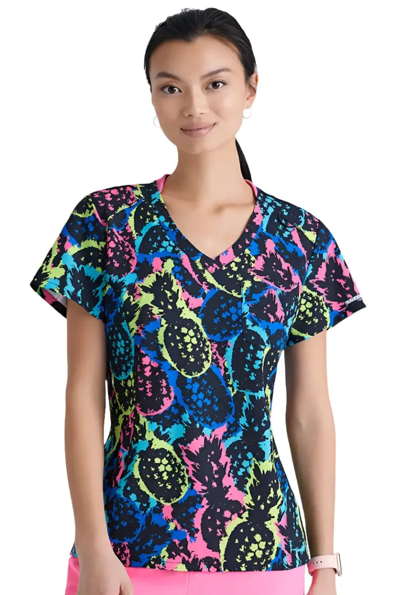 A young female Pediatric Nurse wearing a Skechers Women's Printed Scrub Top in Pineapple Pop featuring short sleeves and a v-neckline.