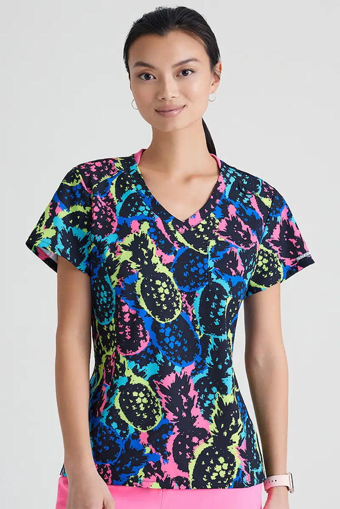 A young female Pediatric Nurse wearing a Skechers Women's Printed Scrub Top in Pineapple Pop featuring short sleeves and a v-neckline.