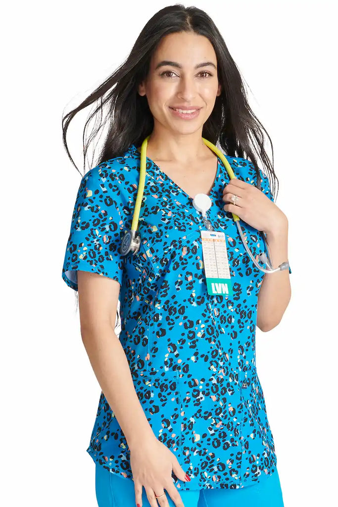 A young female Oncology Nurse wearing a Cherokee Women's Mock Wrap Scrub Top in "Leopard Pops" size Xl featuring 2 front patch pockets for ample storage space.