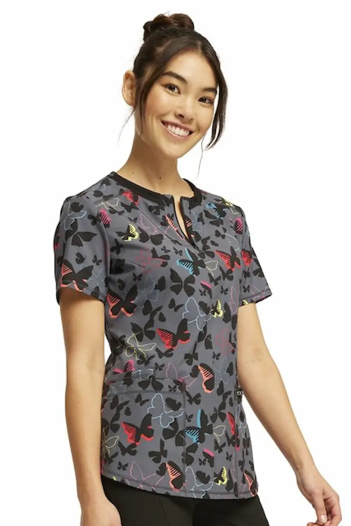 A young female Neonatal Nurse wearing a Cherokee Infinity Women's Round Neck Printed Scrub Top in "Brilliant Butterflies" size XL featuring 2 front patch pockets for ample storage space.
