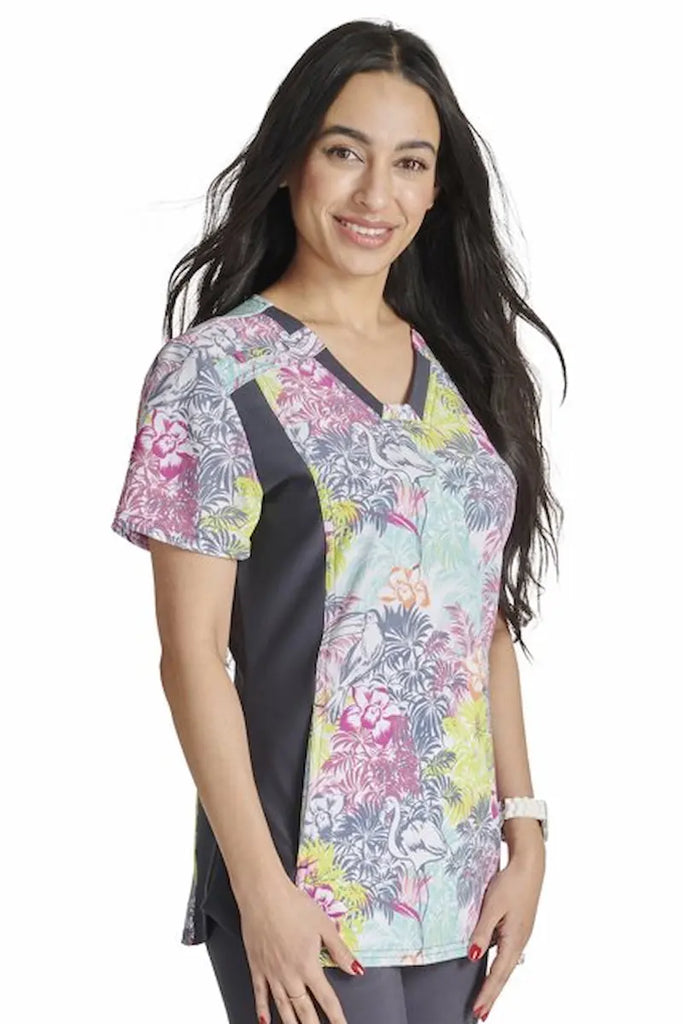 A young female Neonatal Nurse wearing a a Cherokee iFlex Women's Knit Panel Printed Scrub Top in "Birds of Paradise" size XL featuring a curved hemline and side vents.