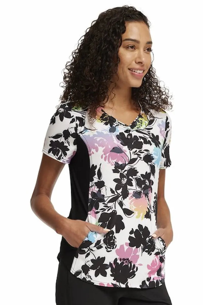 A young female Labor and Delivery Nurse wearing a Cherokee iFlex Women's V-neck Printed Scrub Top in "Garden Glow" size XL featuring 2 in seam pockets for ample storage space.