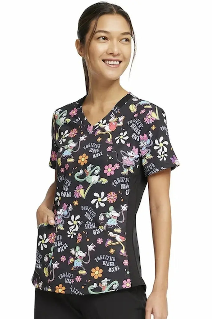 A young female Home Health Care Aide wearing a Tooniforms Women's V-neck Printed Scrub Top in "Positive Vibes" featuring two front patch pockets for amble storage space.