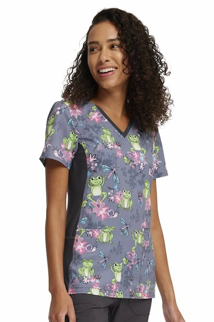 A young female Labor and Delivery Nurse wearing a Cherokee iFlex Women's V-neck Printed Scrub Top in "Toad--ally Floral Friends" size Small featuring a straight hemline.
