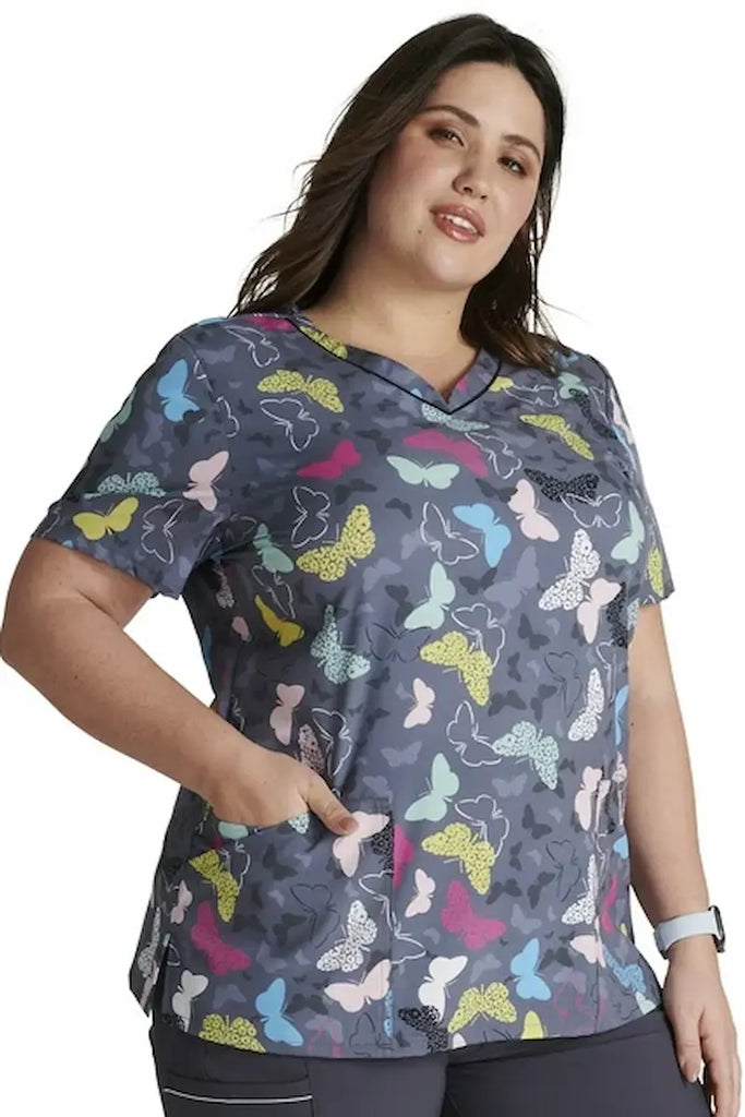 A young female Psychiatric Nurse wearing a Cherokee Women's V-neck Print Scrub Top in "Wing It Up" size Medium featuring a stylish curved V-neckline.