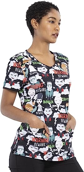A young female Home Health Aide wearing a Cherokee Tooniforms Women's V-neck Print Scrub Top in "Beware of Monsters" size Large featuring side slits for additional range of motion.