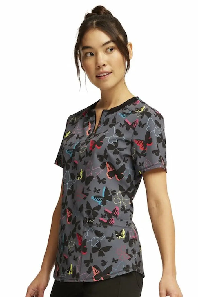 A young female Oncology Nurse wearing a Cherokee Infinity Women's Round Neck Printed Scrub Top in "Brilliant Butterflies" size XL featuring a rib knit neck line with a 1/4 zip closure. 
