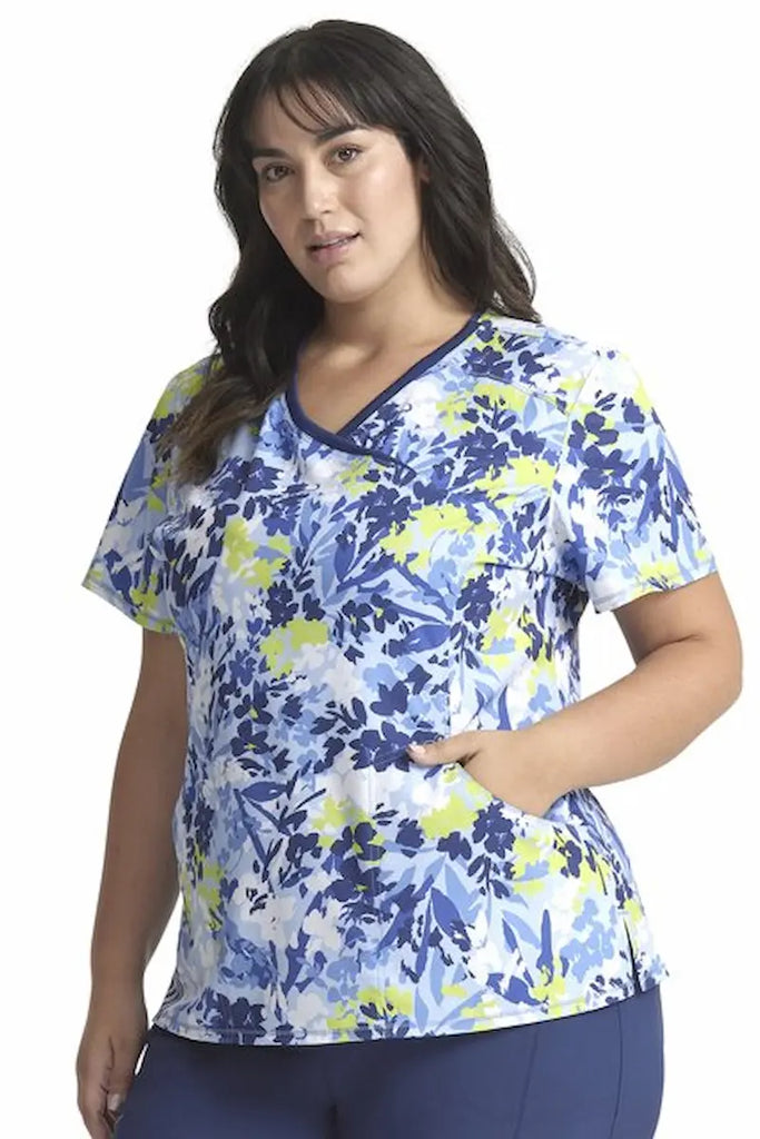 A young female Neonatal Nurse wearing a Cherokee Infinity Women's Mock Wrap Scrub Top in "Brushstroke Buds" size Large featuring princess seaming throughout.