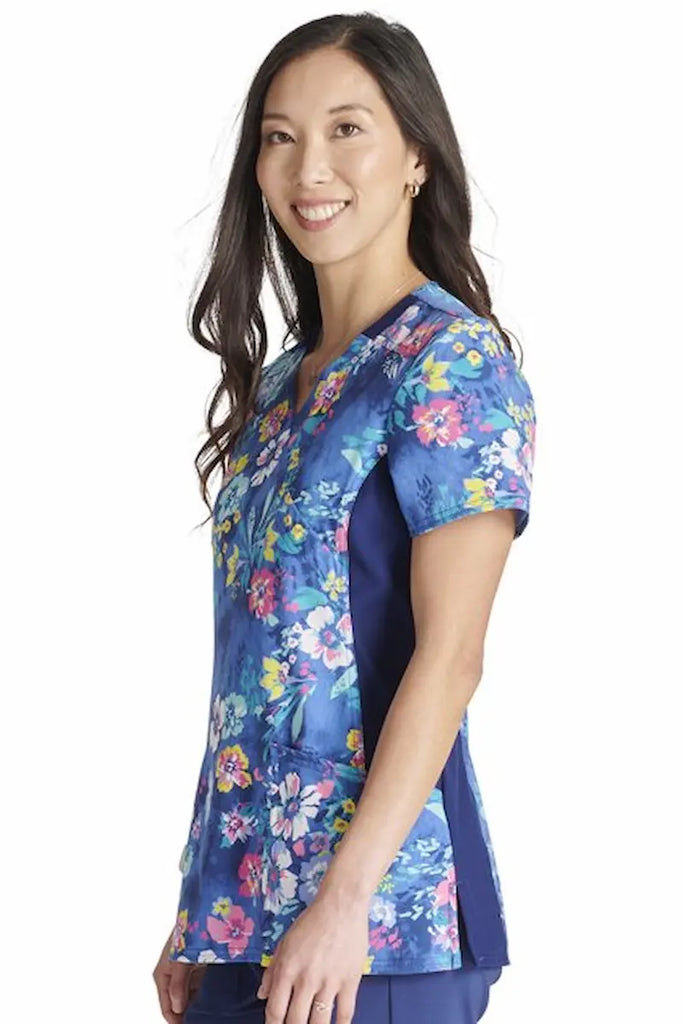 A young female Oncology Nurse wearing a Cherokee Women's Knit Panel Printed Scrub Top in "Blooming Tie Dye" size Large featuring two front patch pockets.