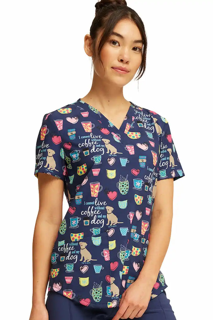 A young female Neonatal Nurse wearing a Cherokee Women's V-neck Printed Scrub Top in "Coffee and My Dog" size 2XL featuring a soft and breathable fabric made of 92% Polyester and 8% Spandex.