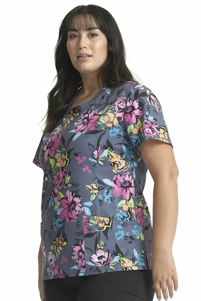 A young female Oncology Nurse wearing a Cherokee Infinity Women's Round Neck Printed Scrub Top in "Electric Blossoms" size 2XL featuring princess seams throughout.