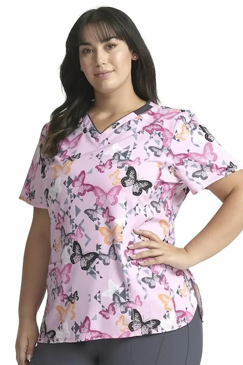 A young female Psychiatric Nurse wearing a Cherokee Infinity Women's V-neck Printed Scrub Top in "Geo Flutter" size Large featuring 2 front angled pockets.