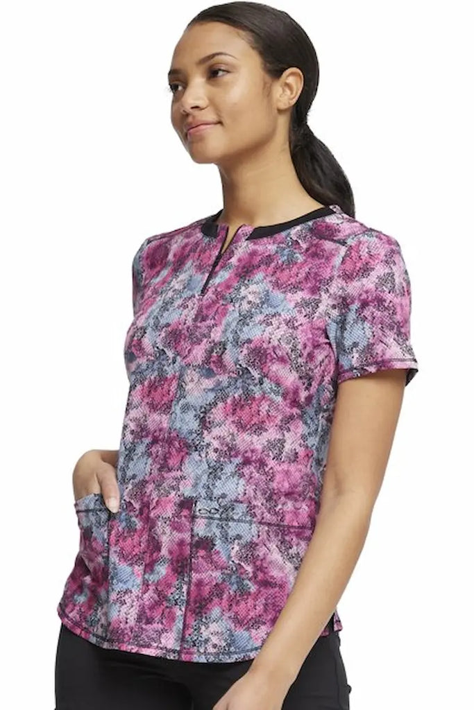 A young female Pediatric Nurse wearing a Cherokee Infinity Women's  Round Neck Printed Scrub Top in size XL featuring 2 front patch pockets.