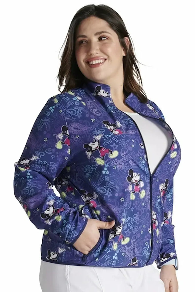 A young female Pediatric Nurse wearing a Tooniforms Women's Packable Print Jacket in "Mickey's Bandana Land" size 2xl featuring a full front zipper closure.