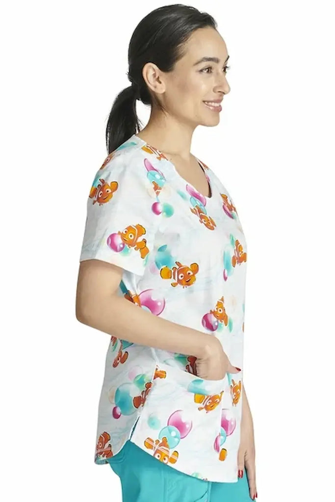 An image of the side of a Home Health Aide wearing a Toonifomrs Women's V-neck Printed Scrub Top in "Nemo Bubbles" size XS featuring 2 front patch pockets for amble storage space.