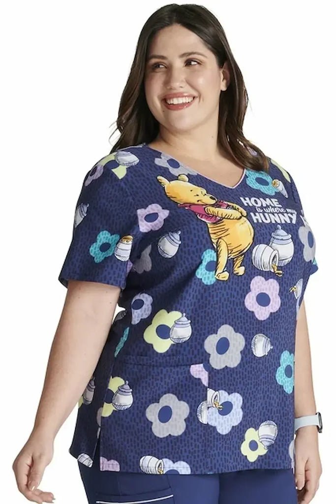 A young female Labor & Delivery Nurse wearing a Tooniforms Women's V-neck Printed Scrub Top in "Home & Hunny" size Large featuring 2 front patch pockets for ample storage space.