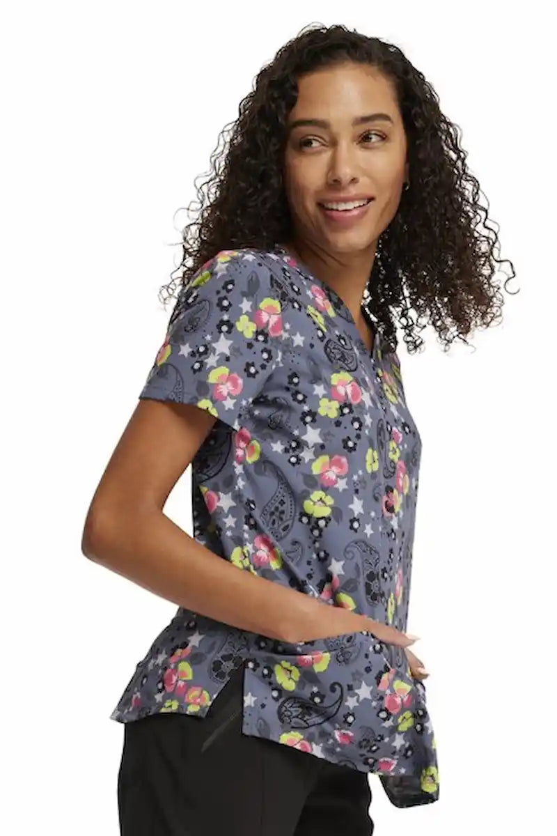 A young female Oncology Nurse wearing a Cherokee Women's V-neck Printed Scrub Top in "Paisley Petals" size Medium featuring side vents for additional mobility throughout the day.