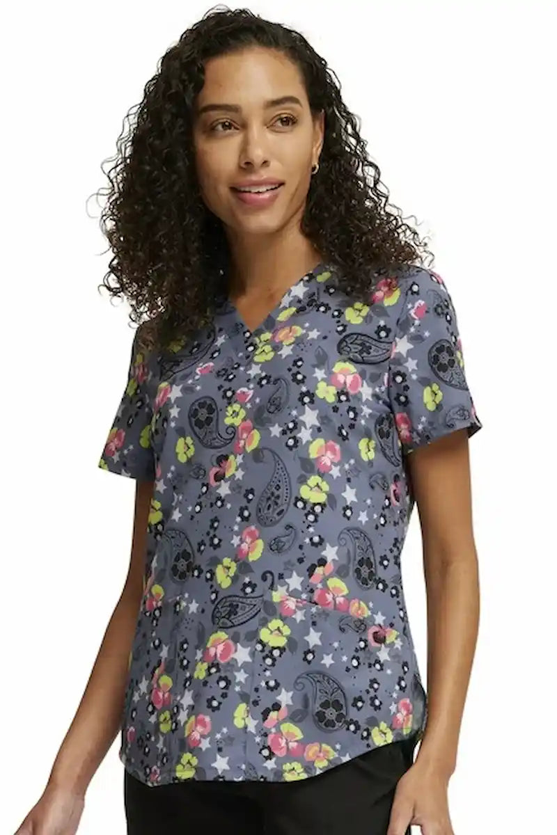 A young female Labor and Delivery Nurse wearing a Cherokee Women's V-neck Printed Scrub Top in "Paisley Petals" size Large featuring two front pockets.